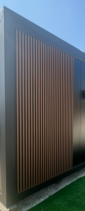 Denne facade har et moderne og stilrent udtryk, hvor lodrette lameller skaber en dynamisk og elegant struktur. De slanke træ- eller træinspirerede lameller står i flot kontrast til de mørkere, glatte overflader, hvilket giver et raffineret og minimalistisk udseende.